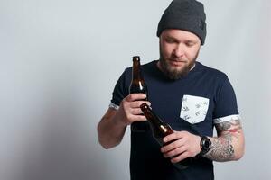 brutal bärtig männlich mit tätowiert Arm Getränke ein Bier von ein Flasche. foto