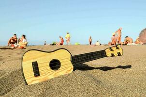 ein hölzern Ukulele sitzt auf das Sand beim das Strand foto