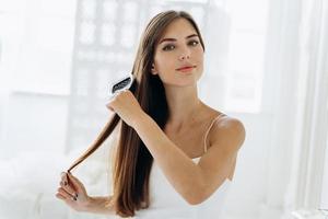 Haare bürsten. Porträt der jungen Frau, die glattes natürliches Haar mit Kamm bürstet. Taille des Mädchens, das schöne lange gesunde Haare mit Haarbürste kämmt. Haarpflege- und Beautykonzept foto