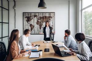 junges attraktives Mädchen, das vor ihren Kollegen einen Bericht macht. Arbeitstreffen im Büro foto