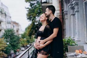 glückliches Paar erwartet Baby, in schwarzer Kleidung posiert auf Terrasse, Balkon foto