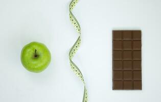wählen zwischen ein gesund Lebensstil und Müll Lebensmittel. Apfel Zentimeter Band und Schokolade auf ein Weiß Hintergrund foto