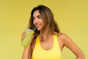 Studio Foto von ziemlich Brünette Frau im sportlich Outfit hoding Getränk und posieren auf Gelb Hintergrund. perfekt schlank Körper.