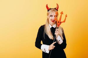 Teufelsfrau, die vor einem gelben Hintergrund steht und die Zunge zeigt foto
