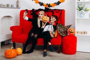 Frau und Sohn haben eine lustige Zeit auf dem roten Sofa und machen ein Selfie. Emotion und Halloween-Konzept foto