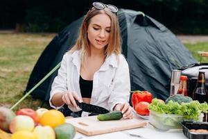 Frau bereitet Essen im Freien auf dem Campingplatz zu foto