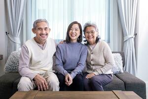 Porträt von asiatisch Familie bestehen von Senior Vater Mutter und Tochter Sitzung zusammen mit glücklich Lächeln auf das gemütlich Couch im Pensionierung Zuhause während Winter zum ältere Pflege zu Ausgaben wertvoll Zeit foto