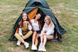 nette Frauen sitzen neben dem Zelt auf dem Campingplatz und posieren vor der Kamera foto