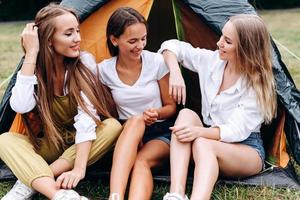 nette Frauen, die neben dem Zelt auf dem Campingplatz sitzen und glücklich lächeln foto