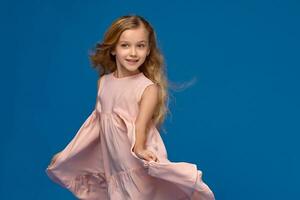 modisch wenig Mädchen im ein Rosa Kleid ist posieren auf ein Blau Hintergrund. foto