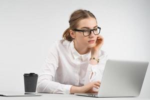Intelligente Geschäftsfrau, die hinter einem Laptop mit einer Tasse Kaffee und einem iPad auf dem Tisch sitzt und sorgfältig arbeitet foto