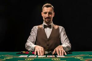 Porträt von ein Croupier ist halten spielen Karten, Glücksspiel Chips auf Tisch. schwarz Hintergrund foto