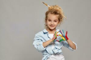 schön wenig Mädchen mit ein gemalt Hände ist posieren auf ein grau Hintergrund. foto