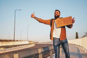 Mann ist Trampen auf Straßenrand versuchen zu halt Wagen. er ist halten Karton mit Inschrift. foto