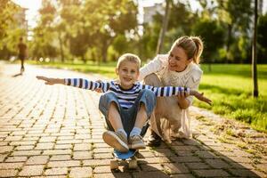 Mutter haben Spaß mit ihr Sohn im Park auf sonnig Tag. Junge ist befreien Skateboard und seine Mutter ist schieben ihn. foto