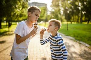 zwei Brüder sind Essen Eis Sahne im Park im Sommer. Sie sind haben Spaß und Verspottung beim jeder andere. foto