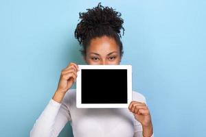 Mockup-Bild eines schwarzen leeren leeren Bildschirms der Tablette in der weiblichen Hand, der hinter dem Tablet auf blauem Hintergrund späht foto