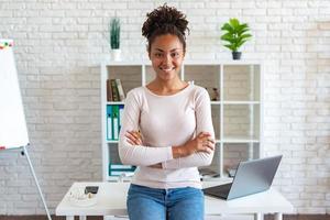 glückliche Frau ruht sich im Büro aus, verschränkte Arme und lächelte in die Kamera, lehnte den Tisch foto