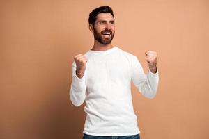 äußerst aufgeregter überglücklicher Mann mit Bart macht Ja-Geste, erstaunt über seinen Sieg, Triumph. Indoor-Studioaufnahme auf beigem Hintergrund isoliert foto