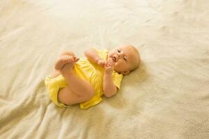 Niedlich, Süss und charmant wenig Mädchen im ein Gelb Bodysuit Lügen auf das Bett und lächelnd. foto