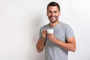 lächelnder Mann steht mit einer Tasse Tee oder Kaffee am Morgen und schaut in die Kamera.- Bild foto