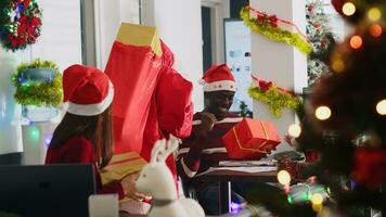 glücklich Mitarbeiter Mitglied Empfang Geschenke von Santa claus im Weihnachten aufwendig Arbeitsplatz. verkleidet Mitarbeiter überraschend ahnungslos Mitarbeiter mit die Geschenke Vor Weihnachten Büro Party foto