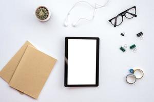 weißer Schreibtisch mit Tablet, Kopfhörer, Notebook, Brille und Schreibwaren - Draufsicht