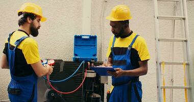 Experte Techniker Mannschaft Arbeiten mit Verteiler Messgeräte zu prüfen Luft Conditioner Kältemittel Ebenen, Schreiben Ergebnis auf Zwischenablage. geschickt Mechanik mit Barometer Benchmarking hvac System Werkzeug foto