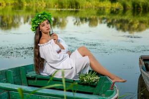 das Nymphe mit lange dunkel Haar im ein Weiß Jahrgang Kleid Sitzung im ein Boot im das Mitte von das Fluss. foto