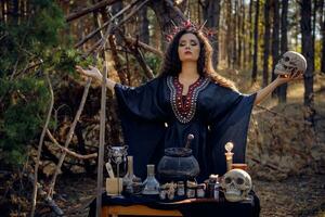 Hexe im Schwarz, lange Kleid, mit rot Krone im ihr lang, lockig Haar. posieren im Kiefer Wald. halten Schädel. Zauber, Magie und Hexerei. Nahansicht. foto