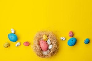 Osterhintergrund, mehrfarbige Eier in einem Nest liegen auf einem gelben Tisch. - Exemplar foto