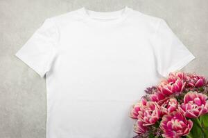 Weiß Damen Baumwolle T-Shirt Attrappe, Lehrmodell, Simulation mit Rosa Tulpen Blumen auf grau Beton Hintergrund. Design t Hemd Vorlage, drucken Präsentation spotten hoch. oben Aussicht eben legen. foto