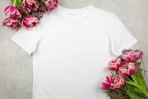 Weiß Damen Baumwolle T-Shirt Attrappe, Lehrmodell, Simulation mit Rosa Tulpen Blumen auf grau Beton Hintergrund. Design t Hemd Vorlage, drucken Präsentation spotten hoch. oben Aussicht eben legen. foto