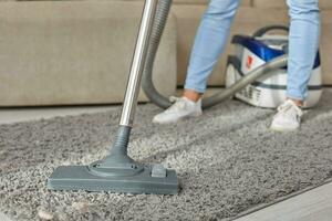 abgeschnitten Bild von schön jung Frau mit ein Vakuum Reiniger während Reinigung Teppich im das Haus foto