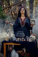 Hexe im Schwarz, lange Kleid, mit rot Krone im ihr Haar. posieren im Kiefer Wald, halten Schädel, Herstellung Trank. Zauber und Hexerei. Nahaufnahme, Rauch. foto