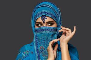 Studio Schuss von ein jung schön Frau tragen das Blau Hijab dekoriert mit Pailletten und Schmuck. Arabisch Stil. foto