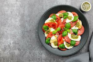 traditionell Italienisch Caprese Salat mit geschnitten Tomaten, Mozzarella, Basilikum, Pesto Soße und würzen auf ein dunkel grau Beton Hintergrund. oben Sicht. Kopieren Raum. foto