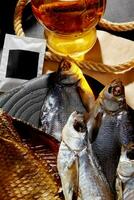 Nahansicht von geräuchert und gesalzen getrocknet Fisch serviert zu Bernstein Lagerbier auf schwarz hölzern Tafel foto