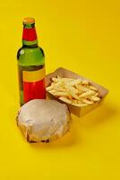 Hamburger im Papier Verpackung, Fritten im Karton Box und Flasche von trinken auf Gelb Hintergrund foto