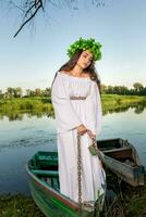 jung Frau mit Blume Kranz auf ihr Kopf, entspannend auf Boot auf Fluss beim Sonnenuntergang. Konzept von weiblich Schönheit, sich ausruhen im das Dorf foto