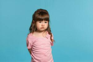 schön wenig Mädchen tragen im ein Rosa T-Shirt ist posieren gegen ein Blau Studio Hintergrund. foto