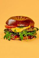Burger mit Kalbfleisch Pastetchen, Käse, Tomaten, Zwiebel und Rucola isoliert auf Pastell- Orange Hintergrund foto