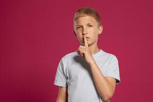 Nahansicht Porträt von ein blond Teenager Junge im ein Weiß T-Shirt posieren gegen ein Rosa Studio Hintergrund. Konzept von aufrichtig Emotionen. foto