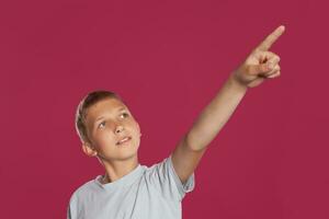 Nahansicht Porträt von ein blond Teenager Junge im ein Weiß T-Shirt posieren gegen ein Rosa Studio Hintergrund. Konzept von aufrichtig Emotionen. foto