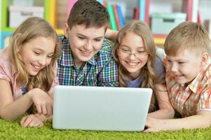 Gruppe von Kinder Lügen auf Fußboden mit Grün Teppich und suchen beim modern Laptop foto