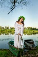jung Frau mit Blume Kranz auf ihr Kopf, entspannend auf Boot auf Fluss beim Sonnenuntergang. Konzept von weiblich Schönheit, sich ausruhen im das Dorf foto
