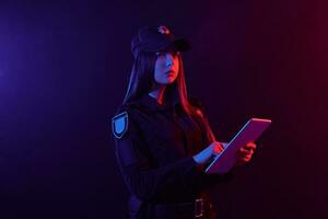 Nahansicht Porträt von ein weiblich Polizei Offizier posieren zum das Kamera gegen ein schwarz Hintergrund mit rot und Blau Hintergrundbeleuchtung. foto