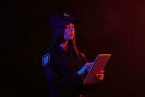 Nahansicht Porträt von ein weiblich Polizei Offizier posieren zum das Kamera gegen ein schwarz Hintergrund mit rot und Blau Hintergrundbeleuchtung. foto