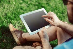 Nahansicht von beiläufig gekleidet jung Mann mit modern Digital Tablette während Sitzung beim das Park, Sonne Licht foto