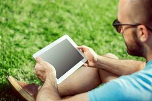 Nahansicht von beiläufig gekleidet jung Mann mit modern Digital Tablette während Sitzung beim das Park, Sonne Licht foto